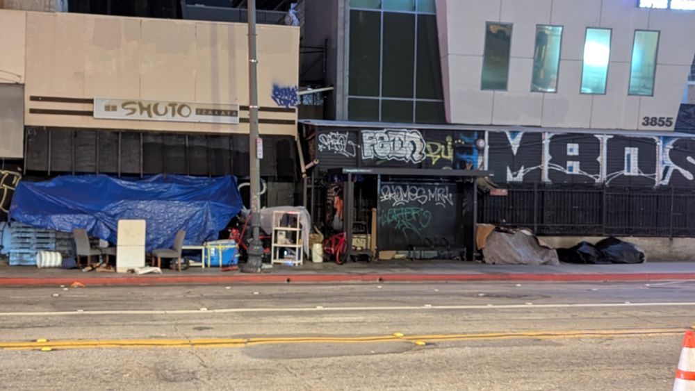 A bus stop for LA Metro's 20 in Koreatown is surrounded by trash, furniture and tarp forts.