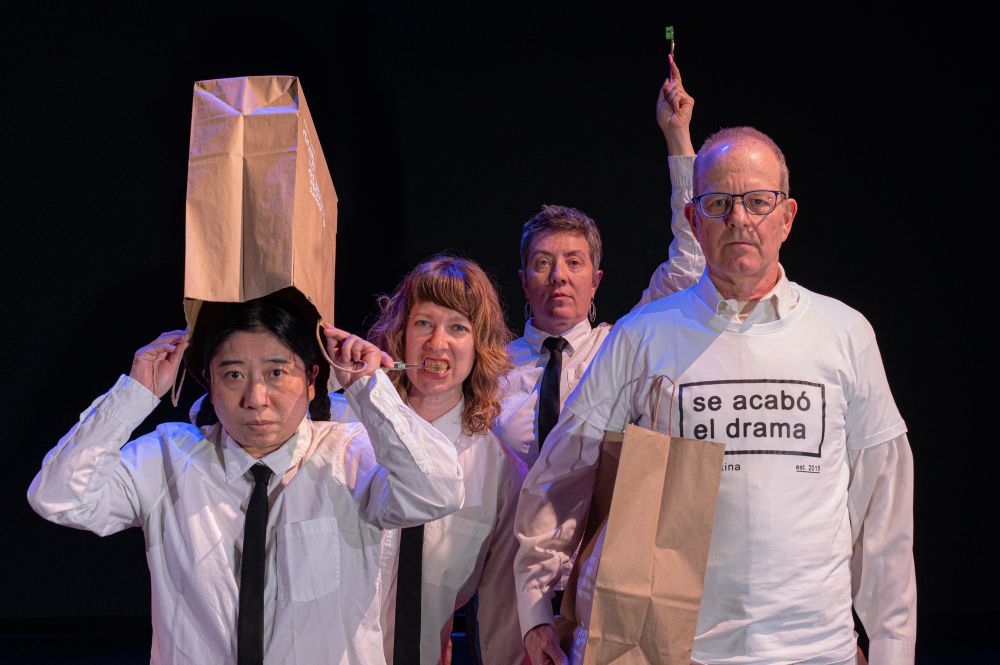 At the left, a woman holds a grocery bag off her head, another woman brushes her teeth behind her and to the right, and behind her holding a toothbrush in the air is third woman. Finally on the right in front is a man holding a grocery bag in his right arm. The women are wearing white dress shirts and black ties. The man is wearing a white t-shirt that reads “se acabó el drama”. All are looking at the camera. Photo: Valerie Oliveiro