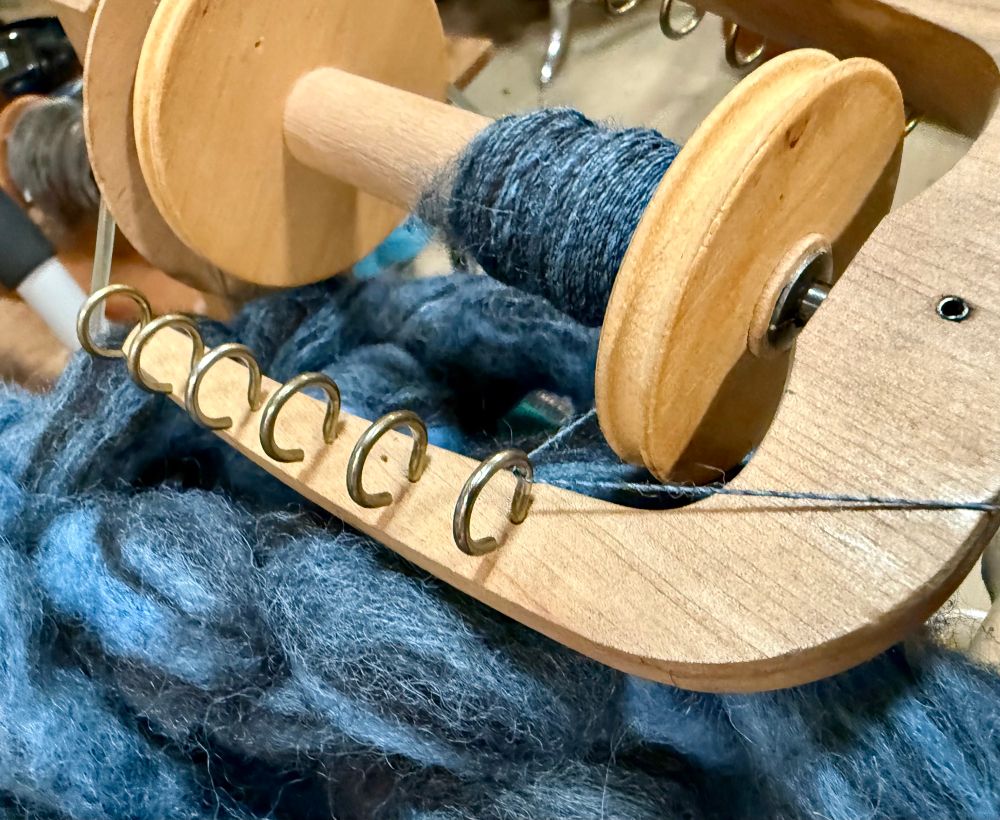 Bobbin of spinning wheel with dark brown and blue fleece in the process of being spun 