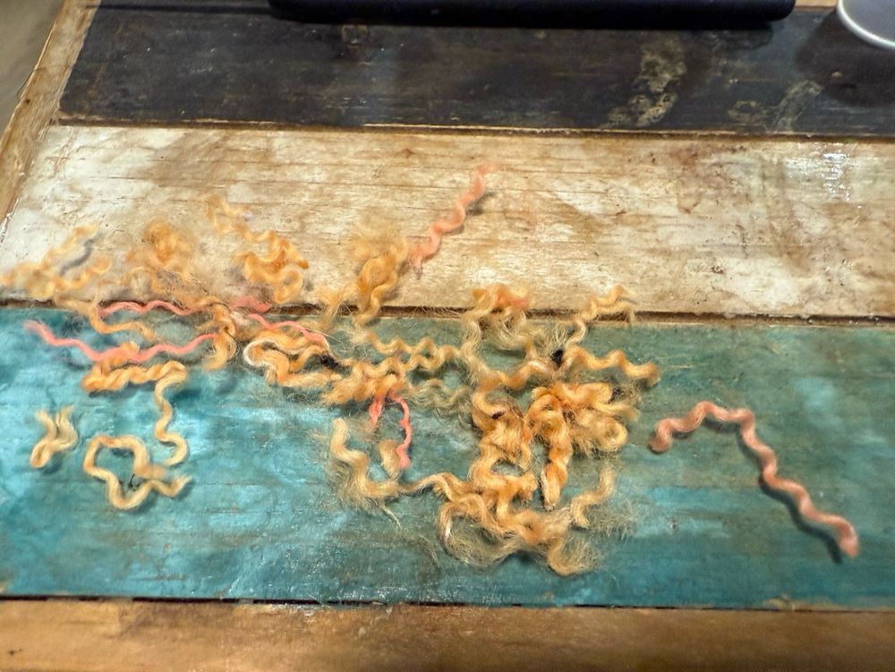 Scraps of orange yarn (multiple shades) split by ply on a multicolored wooden table. The yarn is about one inch in length. 