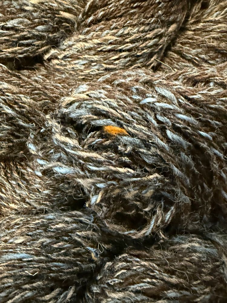 Close up of 3 ply yarn in dark brown, blue, gray with a pop of orange tweed