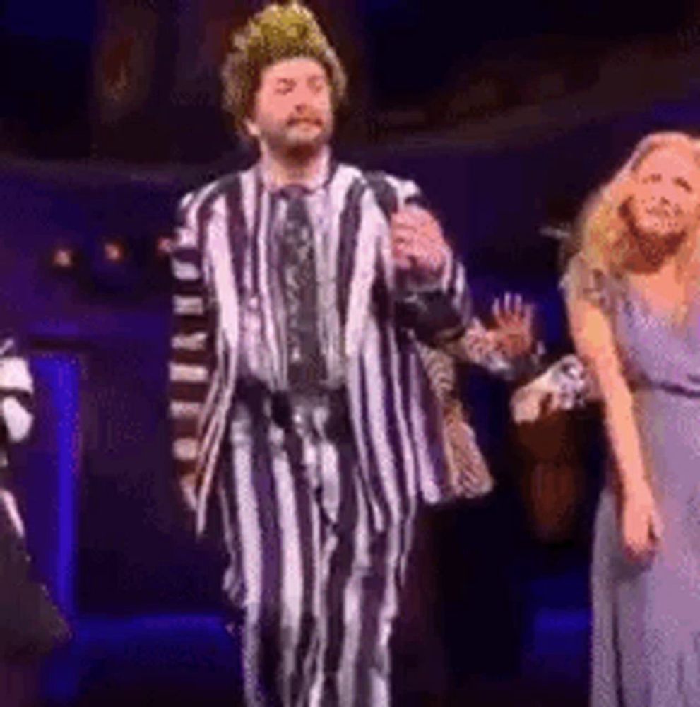 a man in a striped suit is standing on a stage with a woman in a purple dress .