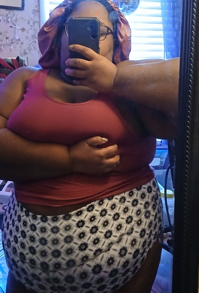 Me in a red tank top and black and white floral booty shorts in front of a mirror 