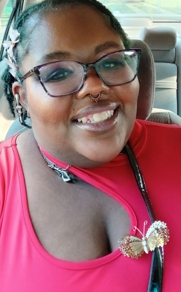 Me in a red top with a gold butterfly pin, a silver necklace, some pretty makeup, a snake earring, red faux nose ring and butterfly hair clips with my glasses on. 