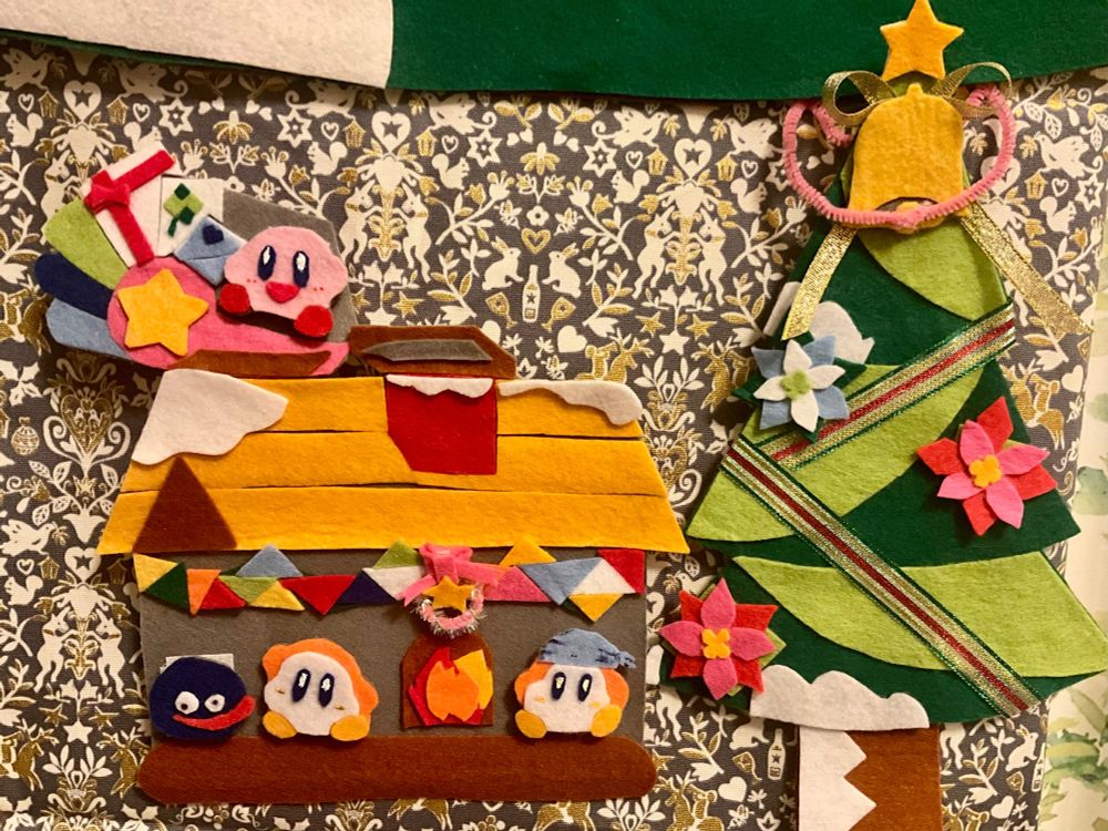 フェルトを使って作られたクリスマス飾りの写真。クリスマスツリーの隣の家の中でワドルディとグーイがいます。屋根の上にプレゼントを乗せたソリにカービィが乗っています。