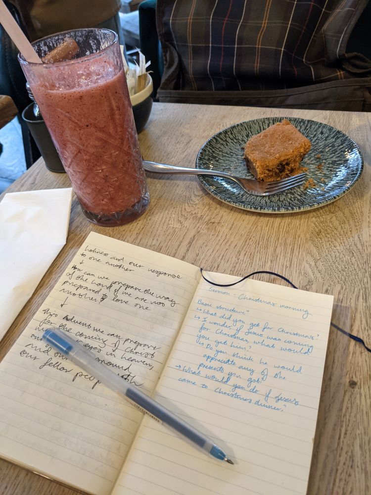 a tabletop in a cafe with a smoothie, a cake and an open notebook