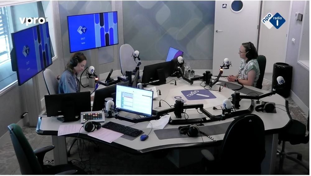 We see a radio studio with presenter Laura Stek facing Nike Stam from behind microphones and computer screens carrying the logo's of Dutch National Public Radio