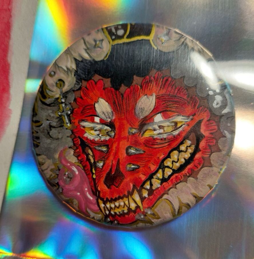 Button badge of a pierced anthro wolf with peeled face and forked tongue.
