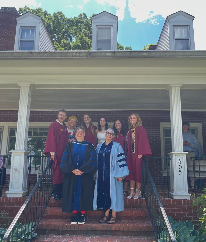 People standing on stairs in front of a house in graduation regalia 