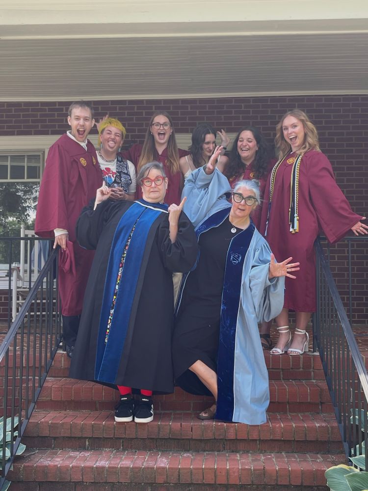 People being silly on stairs in front of a house in graduation regalia 