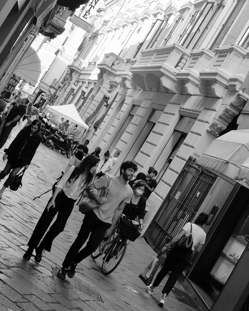 A tilted black-and-white photo of people walking on a pedestrian-only street in a European city.
