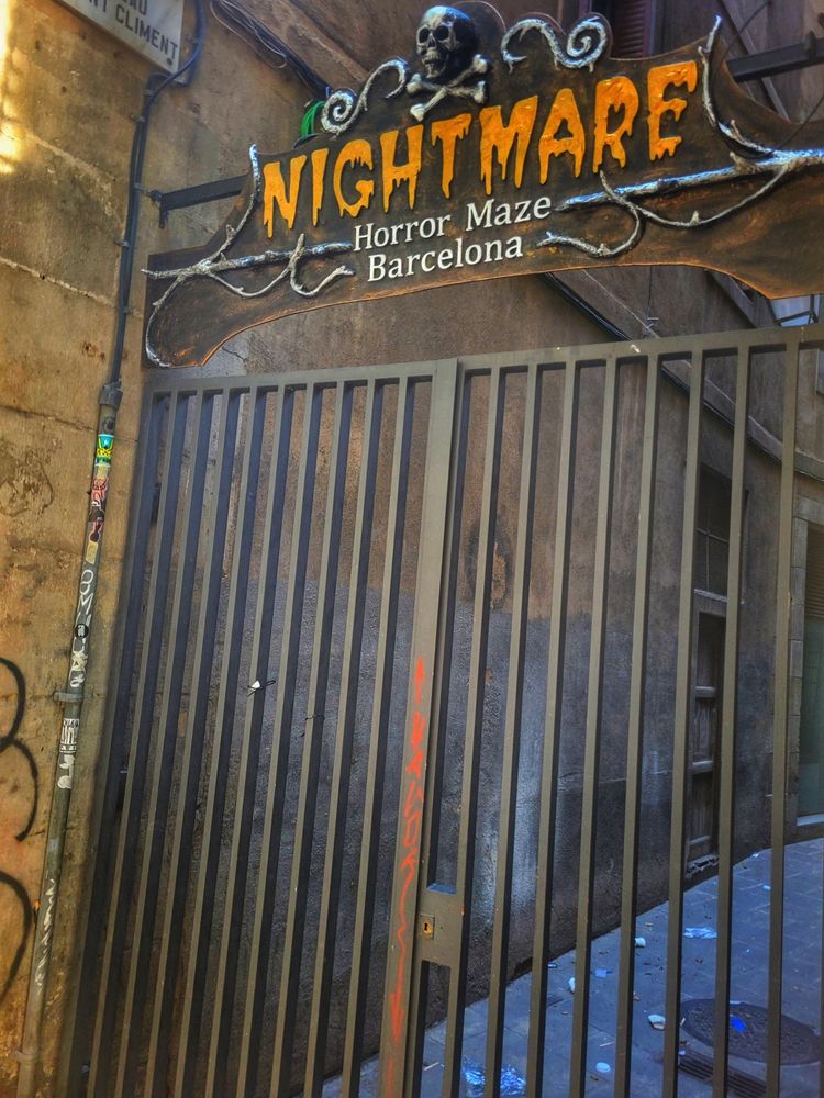 A closed iron gate with a skull and crossbones on top and a sign that reads Nightmare, horror maze Barcelona. 