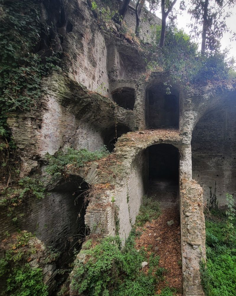 Ruins of an ancient stacked stone building with numerous arched openings, covered with green moss and ivy.
