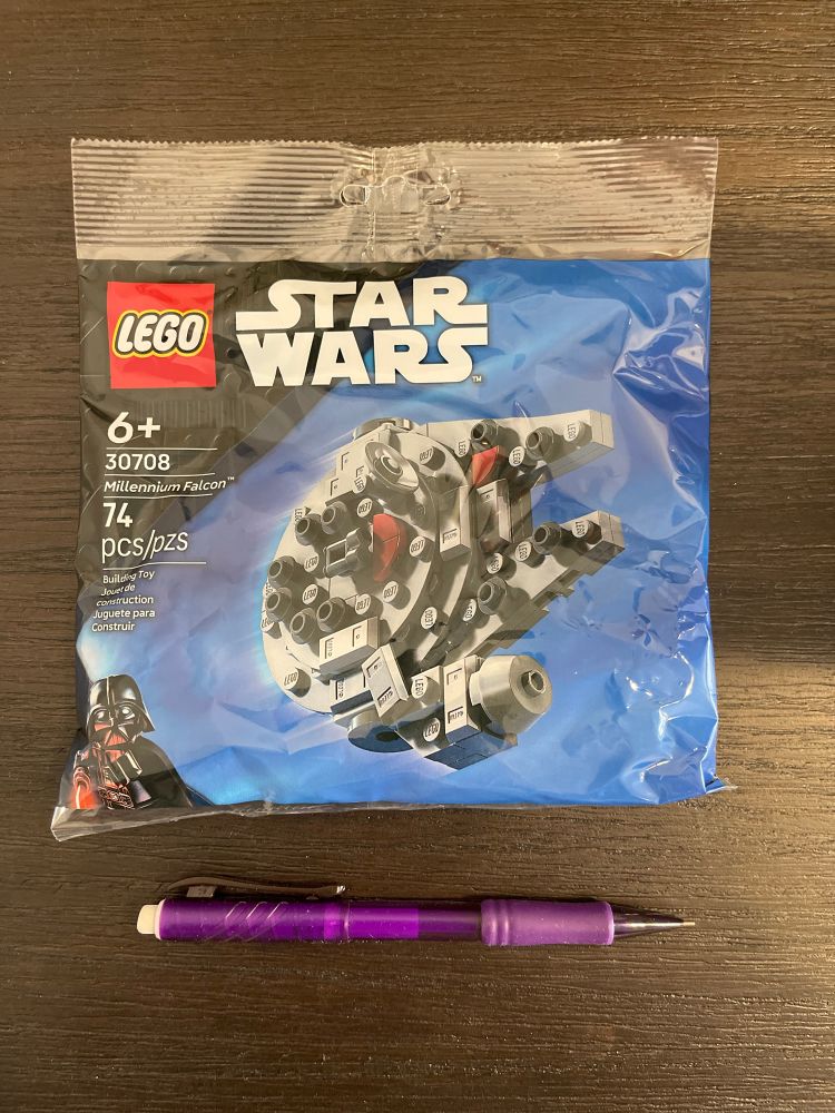 A small bag containing the Lego Star Wars, mini Millennium Falcon set (Set 30708). It contains 74 pieces. Underneath the bag is a purple mechanical pencil for a size reference, which is only slightly shorter than the bag. 