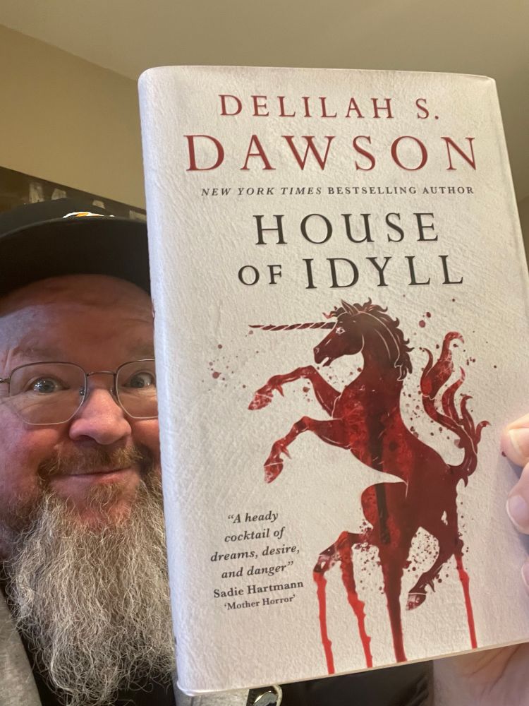 Me holding a copy of HOUSE OF IDYLL, which features a very bloody unicorn on the cover