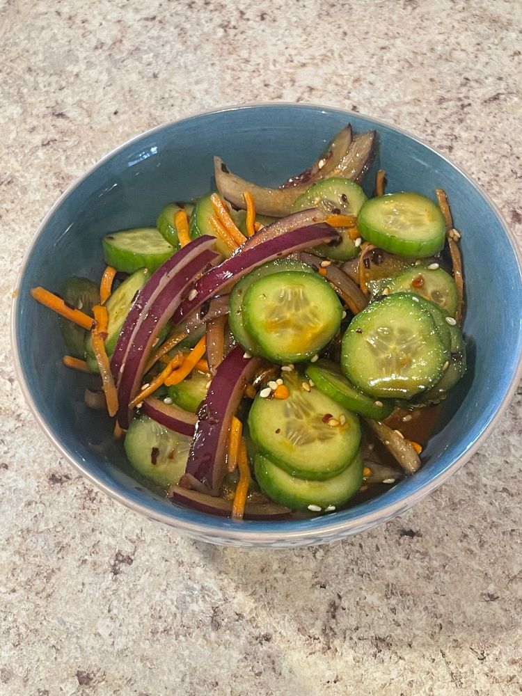 Finished cucumber salad in a bowl, the carrots, onions, and cucumber all glazed in the yummy sauce