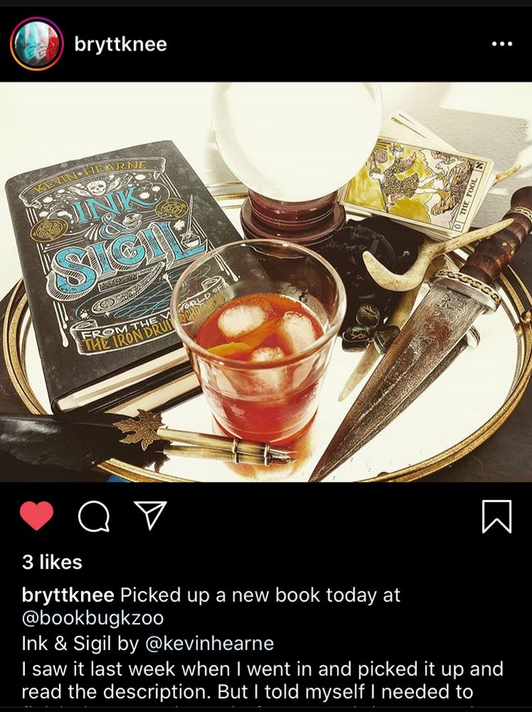 On a silver service tray we see a copy of the book, a glass of whisky on the rocks, a black feather pen, a knife, and a deck of Tarot cards. Caption from bryttknee is partial in the screenshot, but it says: Picked up a new book today. I saw it last week when I went in and picked it up and read the description. But I told myself I needed to