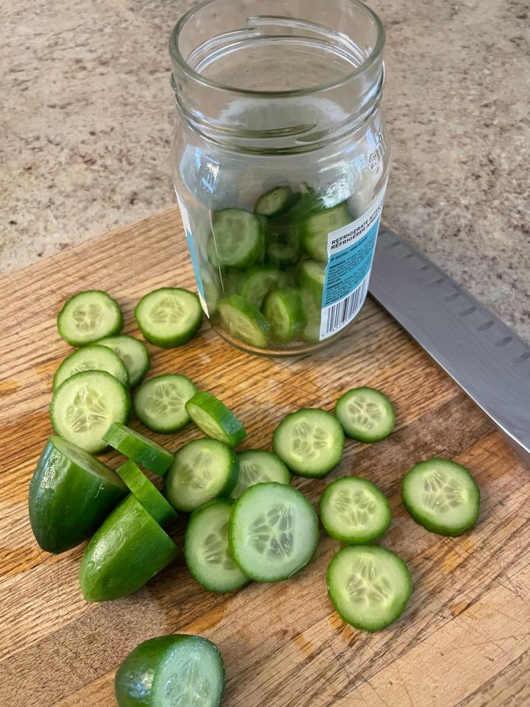 Three mini cucumbers sliced on a cutting board, some of the slices in an old salsa jar