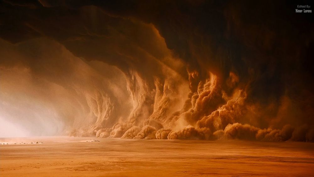 A still of the movie Mad Max: Fury Road showing a group of cars approaching a massive dust storm