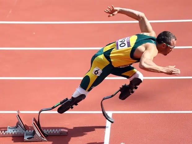 Male athlete runner runs at paralympics with both prosthetic (special for running, curved form) legs. view from the side, pose is very dynamic, both prosthetics are seen