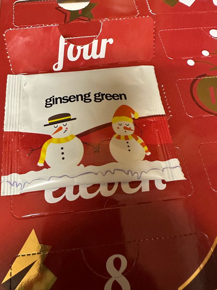 The tea packet lays in front of door 4 on the advent calendar. It says “ginseng green” and has two snowmen in scarves and hats. 