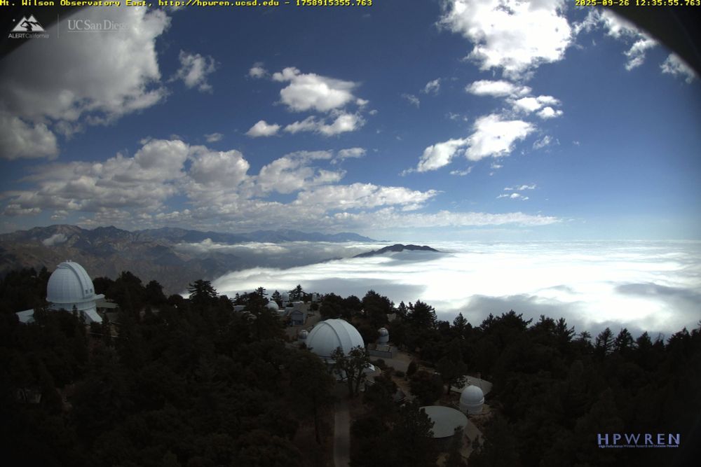 View from atop Mt. Wilson (location: 34.22,-118.06 at 5,620 feet,) from the Observatory, looking East just now. The camera location is basically the Northern edge of Los Angeles, just above Pasadena, and is part of the HPWREN network which includes webcams across Southern California. The network typically provides a N/W/S/E view for each location and time-lapse as well. The view in this image includes the San Gabriel mountains, bright white clouds and the marine-layer covering most of the valley, with the Observatory's 100-inch & 60-inch telescopes and various smaller telescopes and out-buildings in the foreground.