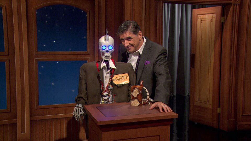 Craig Ferguson and Geoff the Robot (as voiced by Josh Robert Thompson,) from The Late Late Show on CBS, around 2011-2014. They're both standing at Geoff's podium looking cheeky with the studio set as background.