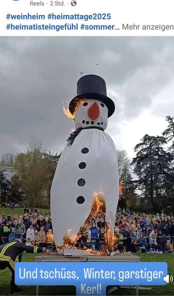 Ein übergroßer Schneemann aus Stoff/Plastik wird angezündet und verbrannt. Menschen stehen außenrum und feiern das Spektakel. 