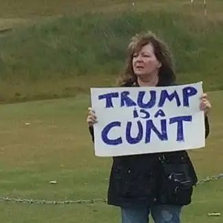 Janey Godley holding up a sign reading "Trump is a cunt"
