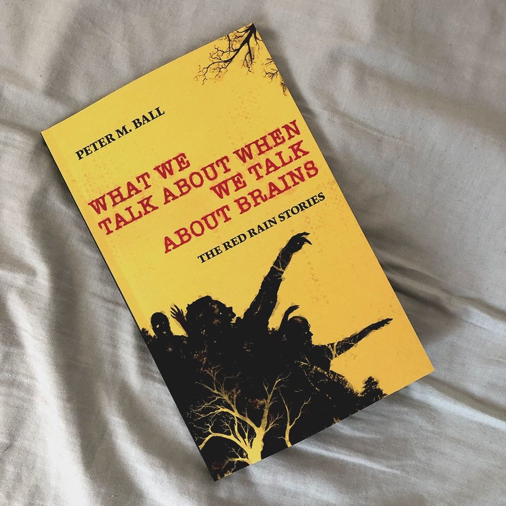 the front cover of Peter M. Ball's What We Talk About When We Talk About Brains, which is a yellow book featuring the silhouette of zombie hordes and the occasional spooky tree. 