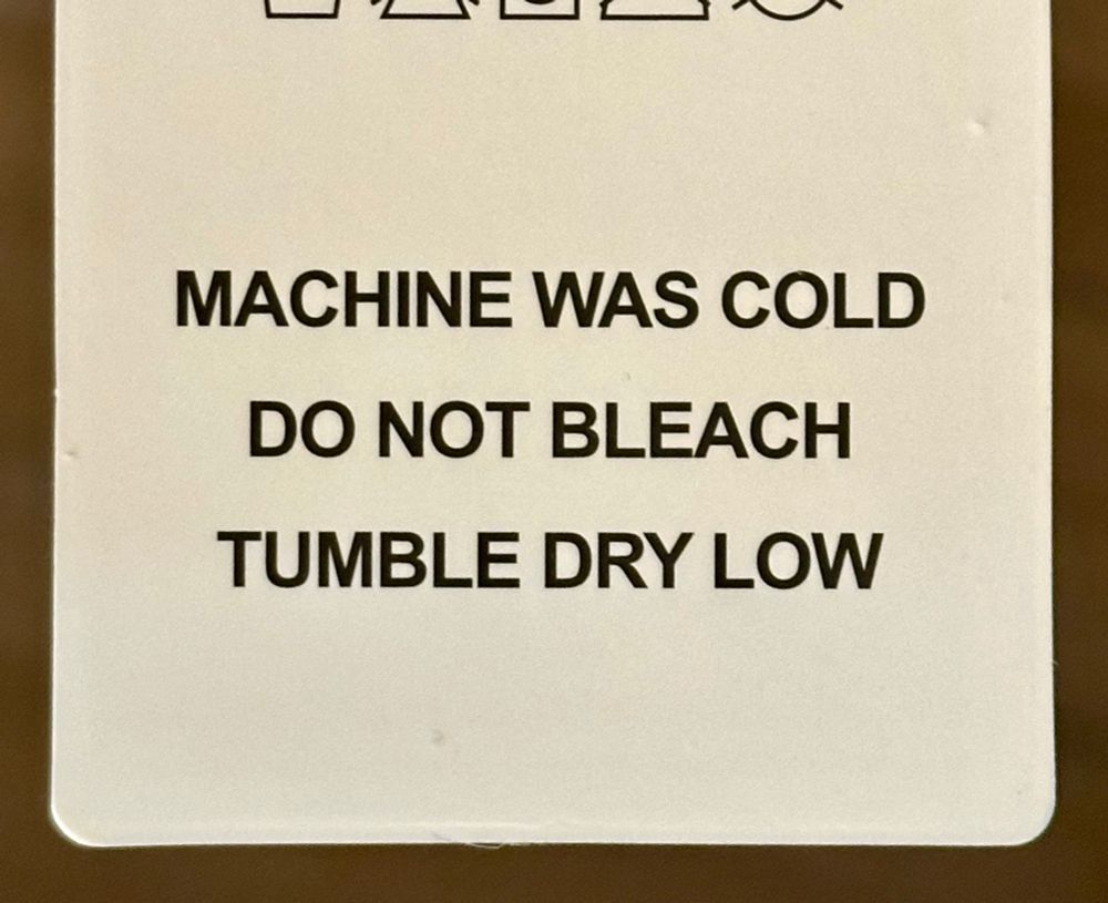 Text on a garment laundry tag that reads “MACHINE WAS [sic] COLD / DO NOT BLEACH / TUMBLE DRY LOW”