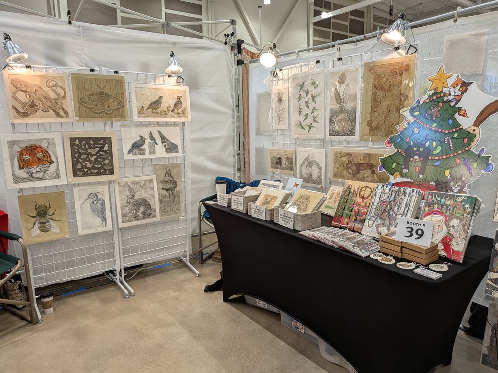Interior of a craft fair booth featuring non-traditional advent calenders and nature themed copper-plate etchings