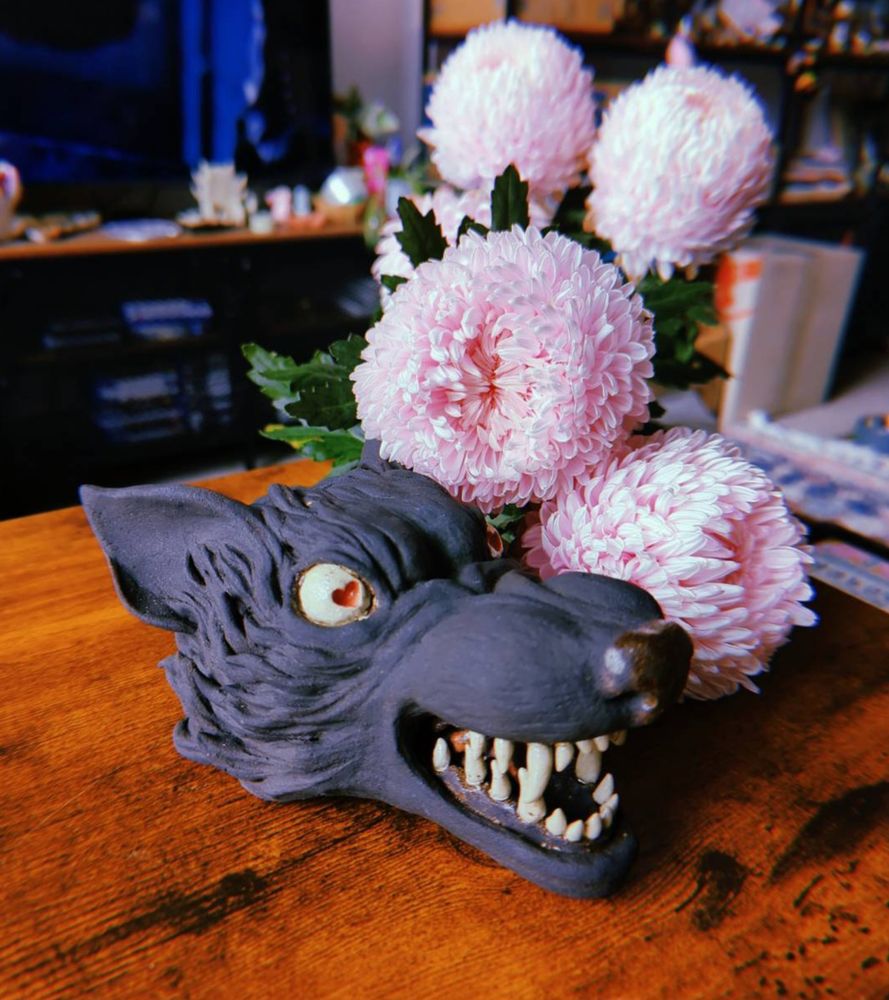 a sculpture of a black wolf head with white eyes and teeth; the eyes have small red hearts in them 