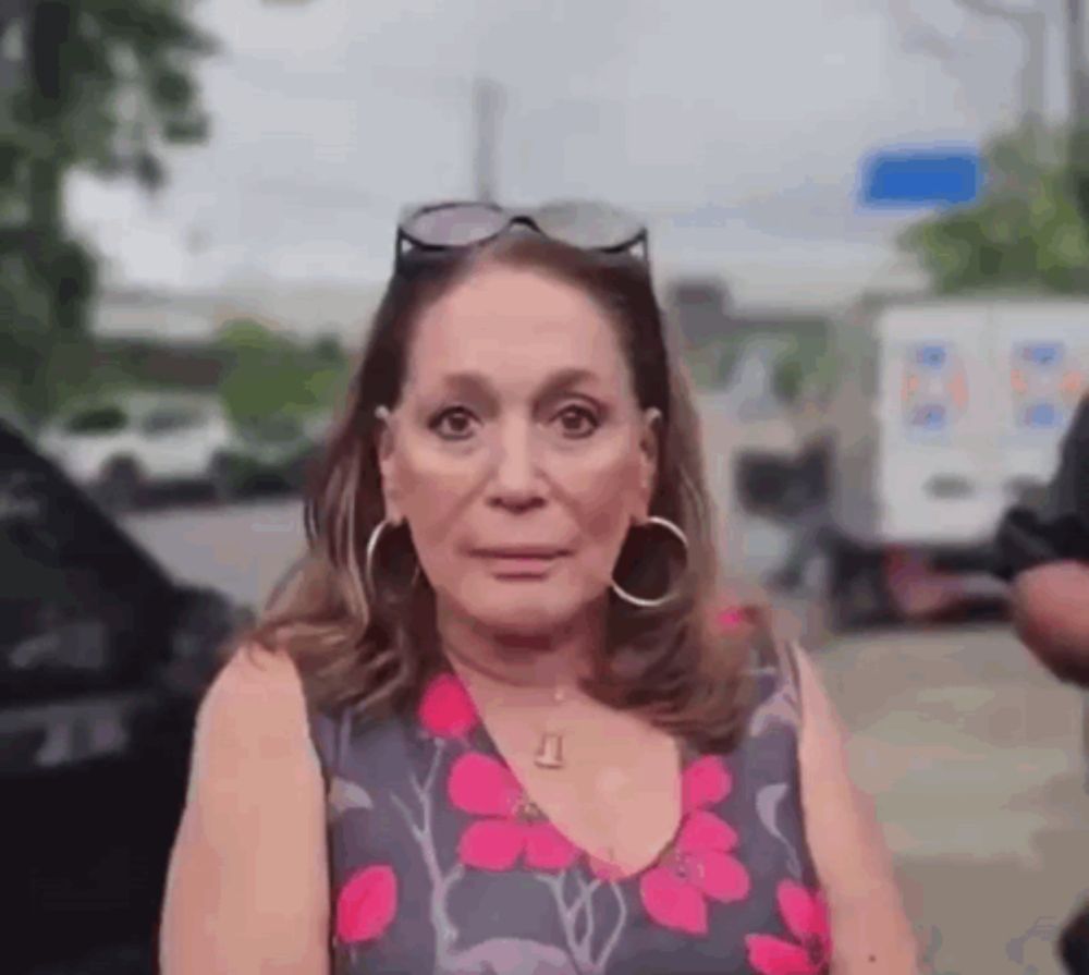 a woman wearing a floral dress and hoop earrings is standing in front of a car .