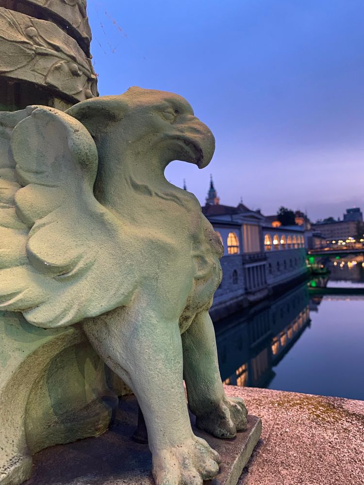 A patina green griffin  perches on the Dragon Bridge overlooking evening reflections of illuminated buildings on the Ljubljanica River in Ljubljana, Slovenia 
