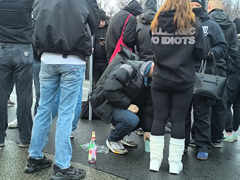 Man sieht die Rechtsradikalen. Vor ihnen auf dem Boden steht eine große leere Likör-Flasche