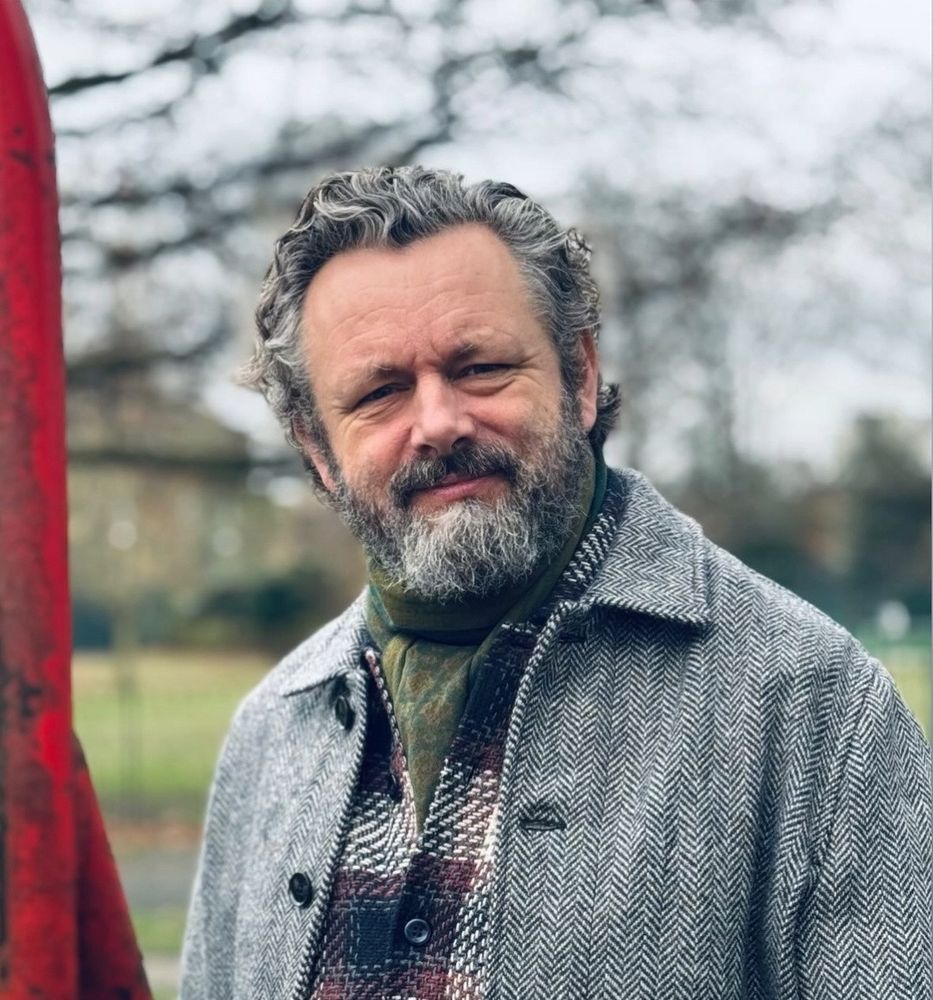 Michael Sheen in a winter coat and green scarf.