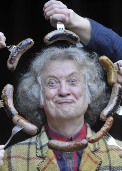 Noddy Holder pulling a face while people with forks hold eight sausages around his head in a circle
