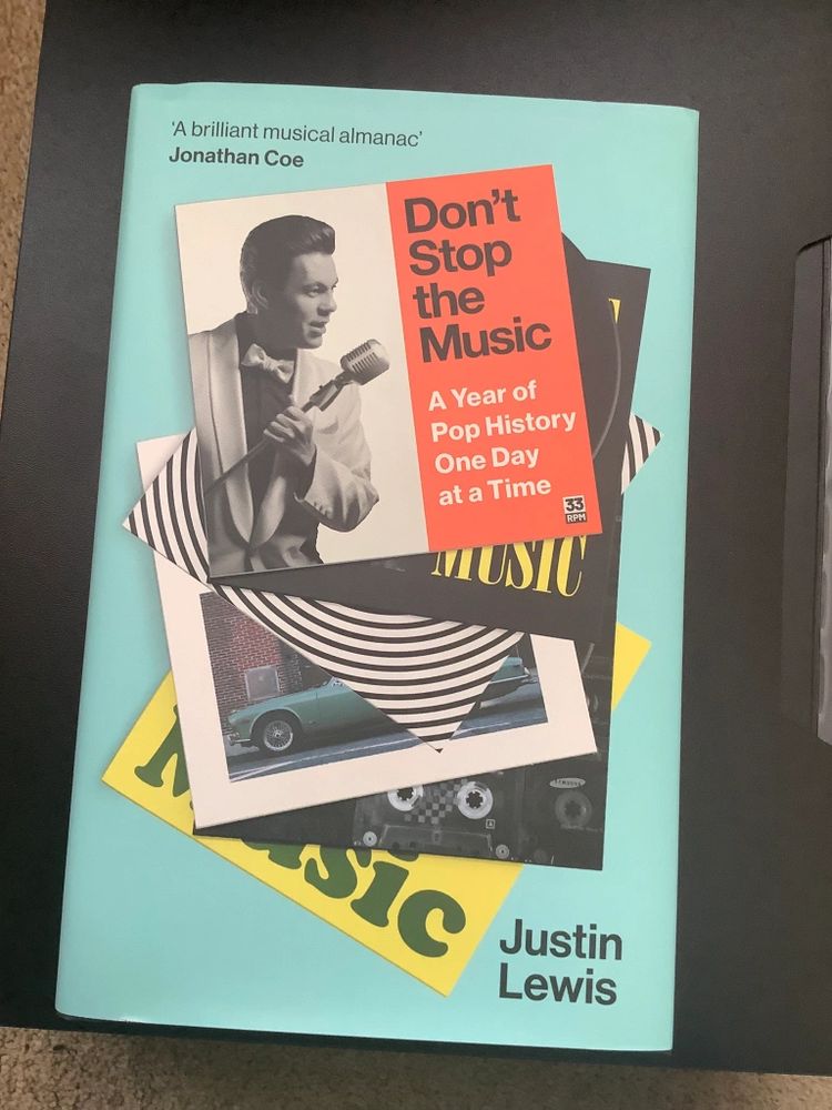 Front cover: Don’t Stop the Music: A Year of Pop History, One Day at a Time, by Justin Lewis, featuring the author in a dinner jacket and bow tie singing into an old microphone on a mocked up record sleeve in a pile of other records