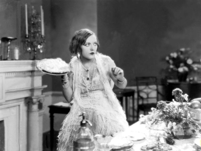 Mabel Normand about to throw a custard pie. Image shows a smartly dressed woman with a cream/custard pie on a plate
