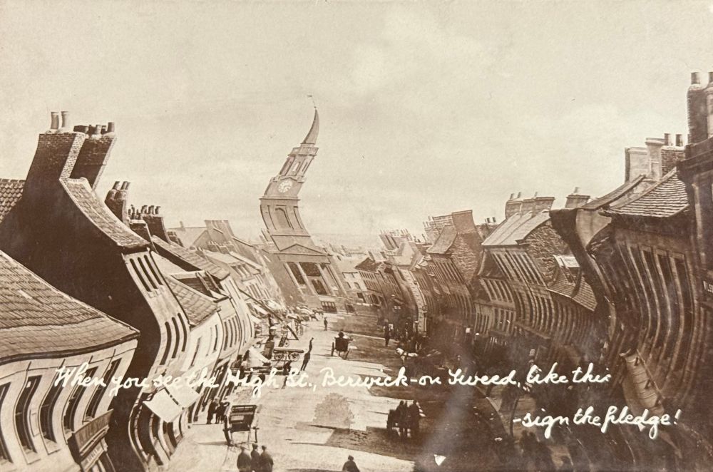 Black and white photographic postcard looking down a street with wiggly buildings with a tall spire at the end of the street, the image twisted during printing. Caption reads: ‘When you see the High Street, Berwick-on-Tweed like this - sign the pledge!’