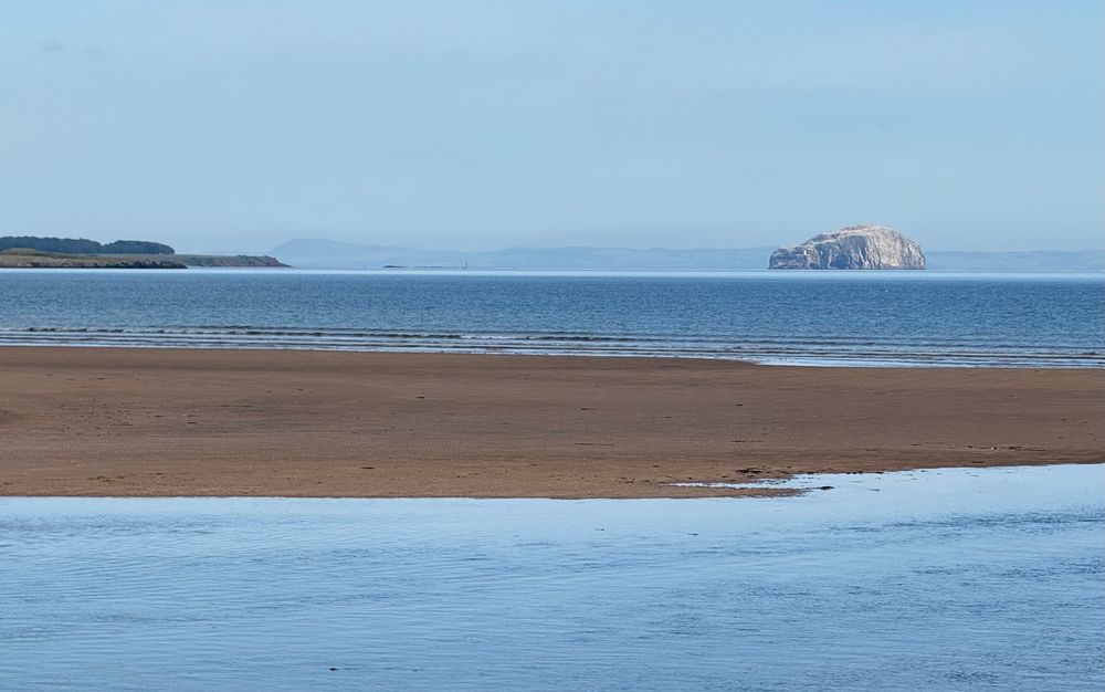 A distant island in a calm sea with a sandbank in the foreground.