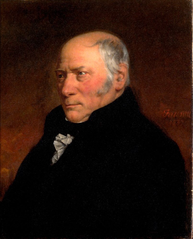 Portrait of William Smith wearing a dark coat. Grey hair and long sideburns fringe his bald head and ruddy cheeks and he has a stern expression.