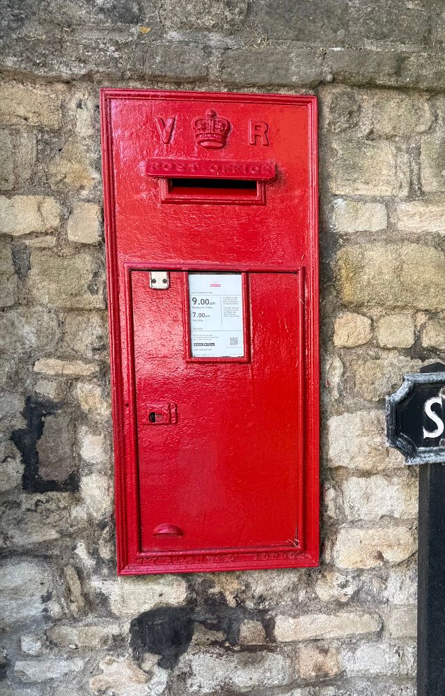 Red postbox with a VR cypher and crown set in a stone wall. 