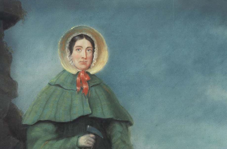 Portrait of Mary Anning wearing a green cloak and a straw bonnet tied with a red ribbon.