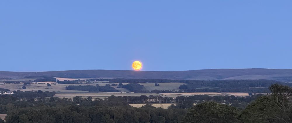 Moon rising over a low range of hills.