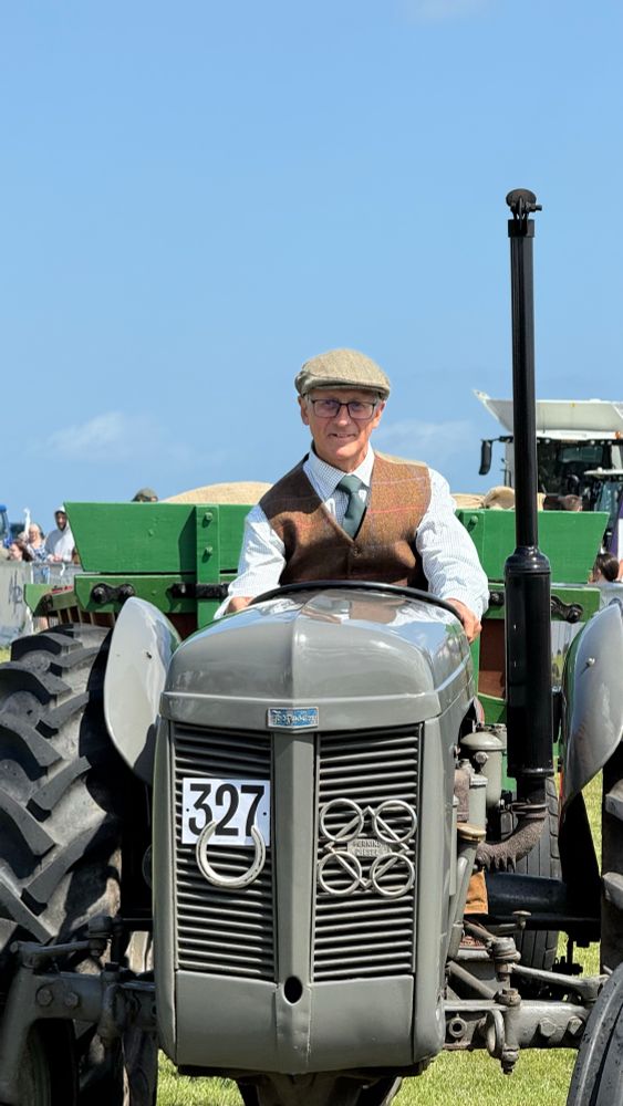 A vintage tractor driven by a man in a tweed cap and waistcoat. 