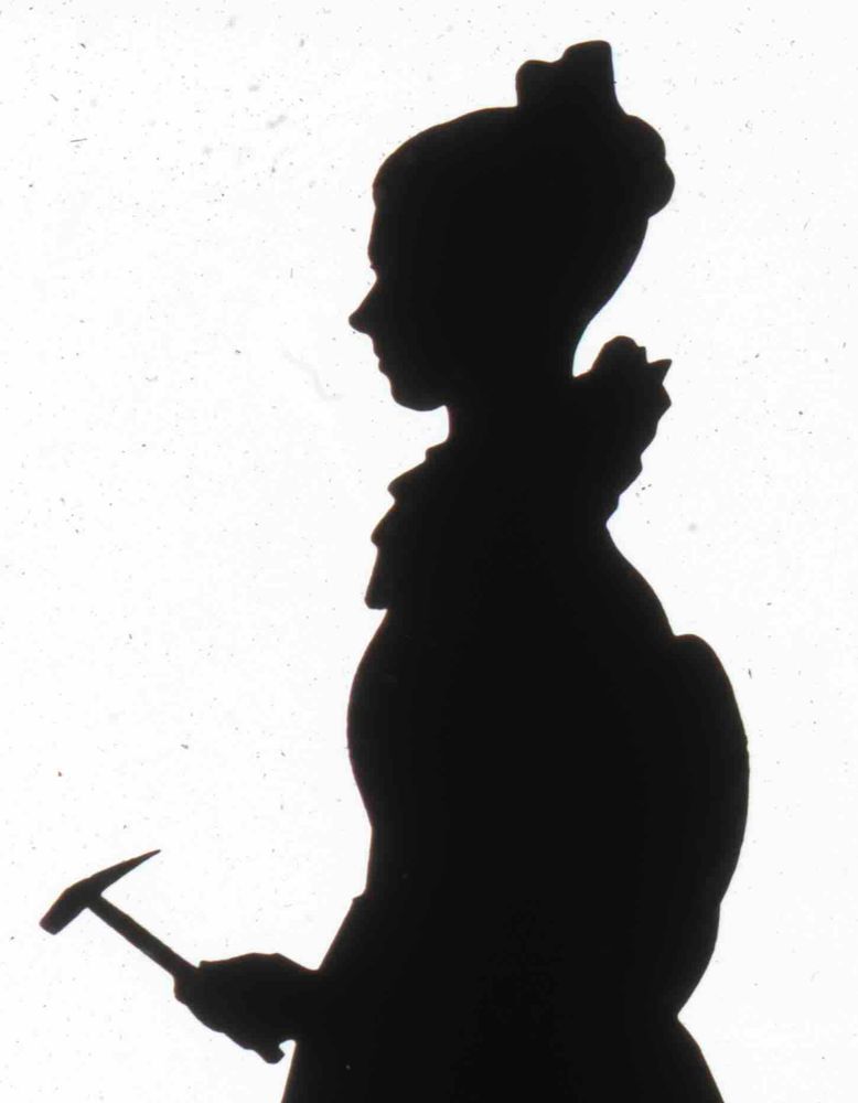 Cut paper silhouette of Mary Anning, c.1831. She wears a dress with a high ruffled collar and full sleeves, has her hair tied in a knot on top of her head and holds a small hammer.