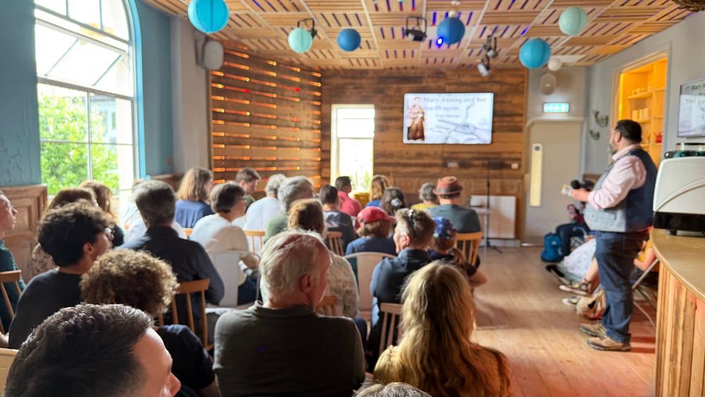 Wood panelled room with an audience looking towards a screen. 