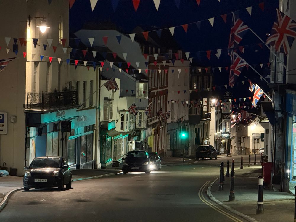 Night view downhill on Broad Street, Lyme Regis with flags and bunting. 